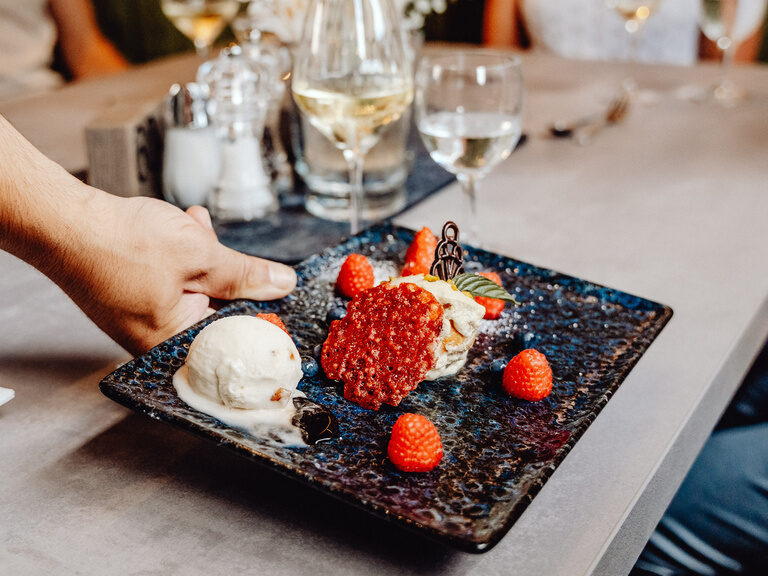 Köstliches Dessert auf edler Tafel Ein Dessert auf einem Tisch mit einem Weinglas im Hintergrund.