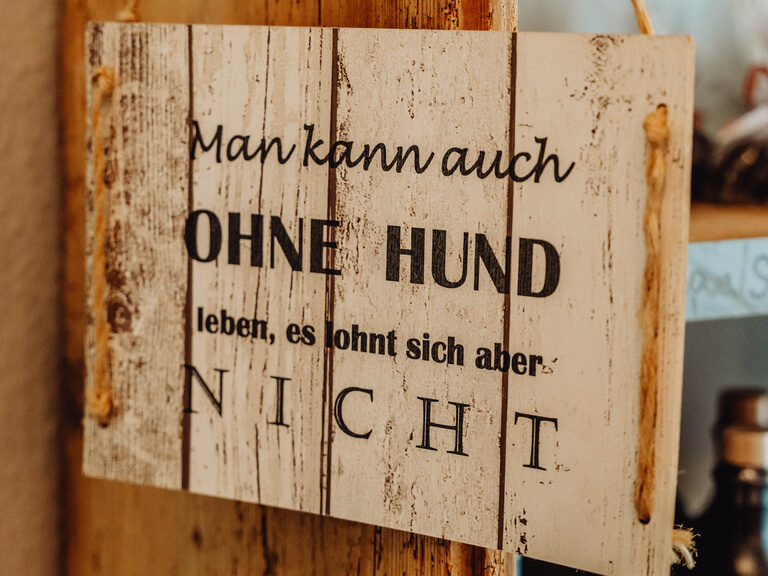 Ein Holzschild hängt neben einer Tür und trägt eine klare Botschaft.